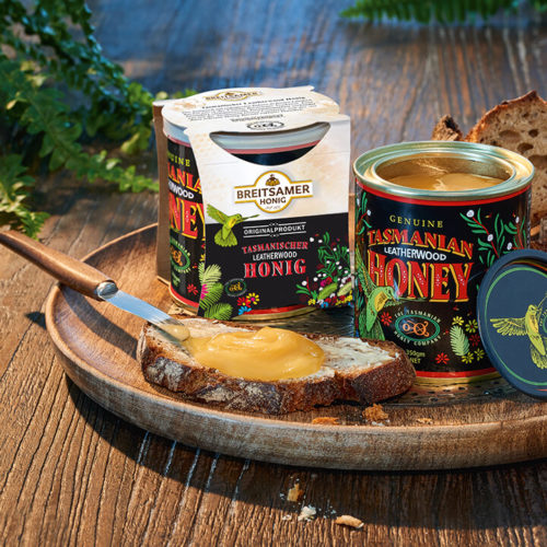 Holztablett mit zwei Dosen Breitsamer Tasmanischer Leatherwood Honig, daneben eine Scheibe Brot bestrichen mit Honig