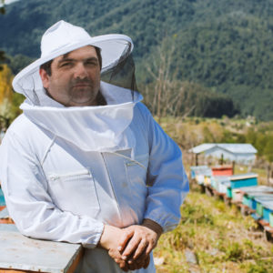 Fairtrade beekeeper in white beekeeper suit leaning against beehive