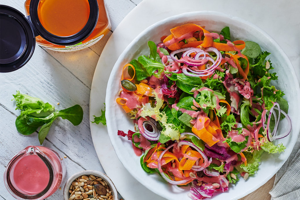 Honig-Senf-Dressing auf weißem Tisch mit buntem Salat