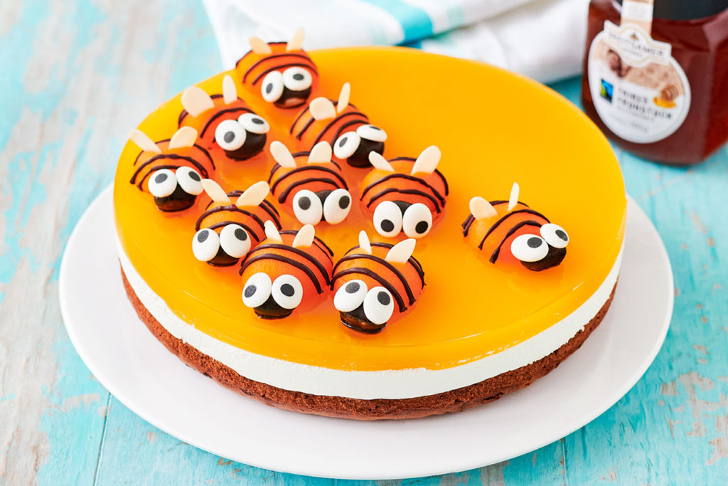 Teller mit einem Kuchen, der mit kleinen Deko-Bienen dekoriert ist. Im Hintergrund ein Glas Breitsamer Faires Frühstück Blüte flüssig