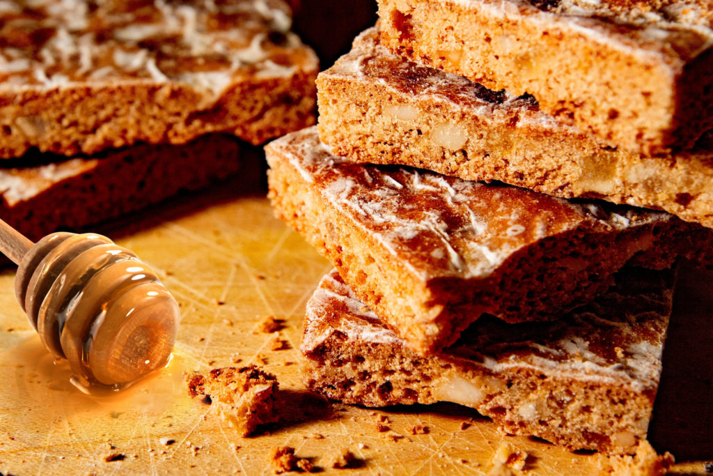 Honig Lebkuchen geschnitten, daneben ein Honiglöffel mit etwas Honig, der herunterläuft