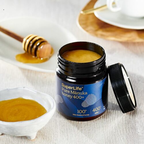 Geöffnetes Glas Breitsamer SuperLife Manuka Honig neben zwei kleinen Schalen mit Honig, in einer Schale liegt ein Honiglöffel