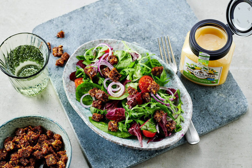 Teller mit Salat, daneben ein Glas Breitsamer Frühlingssumen und eine Schale mit knusprigen Honig-Croutons. 